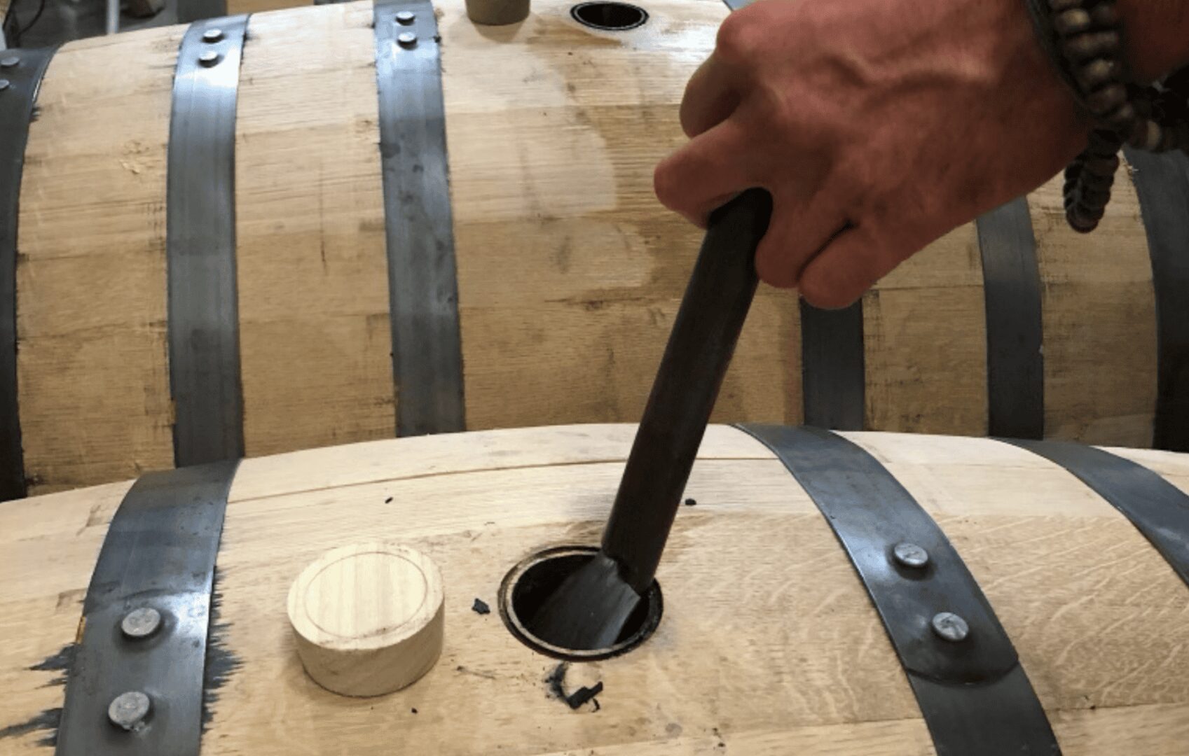 Person extracting whiskey from a wooden barrel.